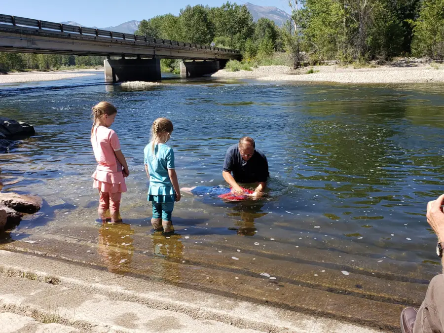 Two girls watch as a child is baptized in the Bitterroot River