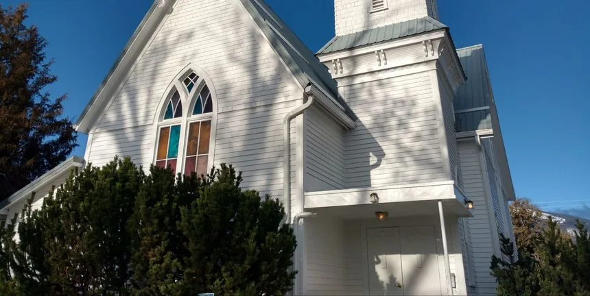 The white wooden church building of Grace Gospel Fellowship with its stained glass window and bell tower