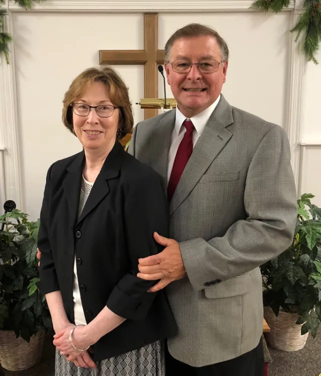 Pastor Jerry Elwell and his wife Tavia standing together in front of the cross at Grace Gospel Fellowship
